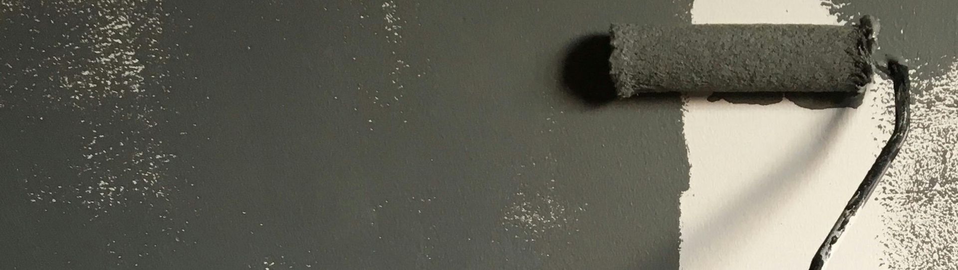 A hand painting a wall gray with a roller during a house renovation project.