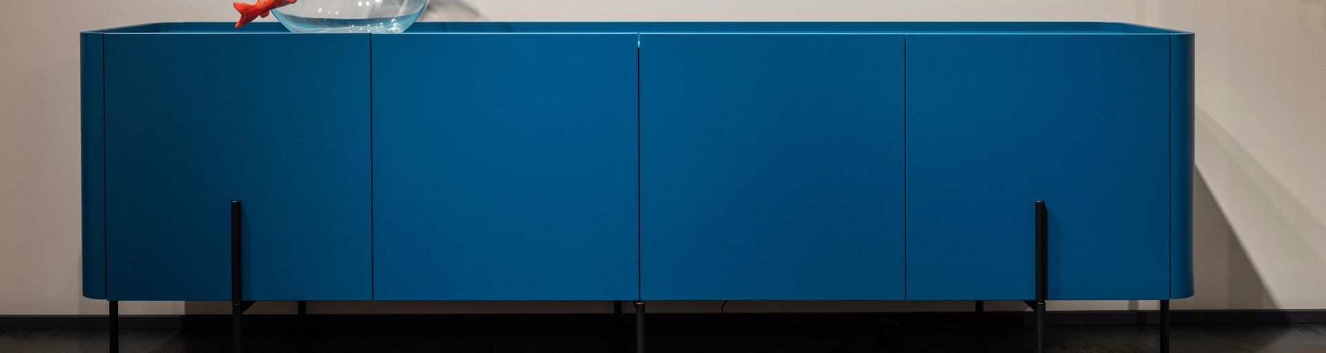 Contemporary interior featuring a fishbowl on a blue cabinet, vibrant wall art, and elegant lighting.